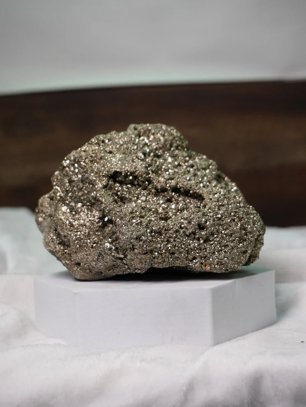 Natural Pyrite stone with metallic crystalline formations, resting on a white display stand